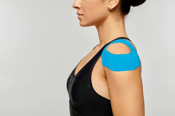 Обрезанный вид молодой женщины в спортивной одежде позирует в профиль с кинезиологическими лентами на плече — стоковое фото