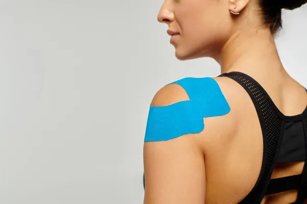 Cropped view of young woman in black sport outfit posing with kinesiological tape on her shoulder — Stock Photo
