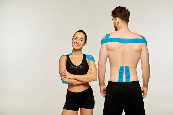 Cheerful woman posing with arms crossed arms on chest next to sporty man, kinesiological tapes — Stock Photo