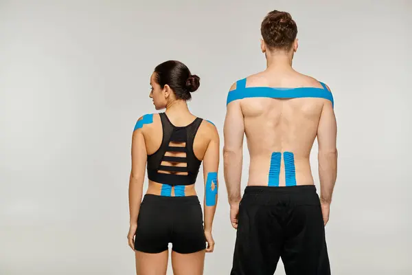 Back view of attractive woman and man in black sport outfits posing with kinesiological tapes — Stock Photo