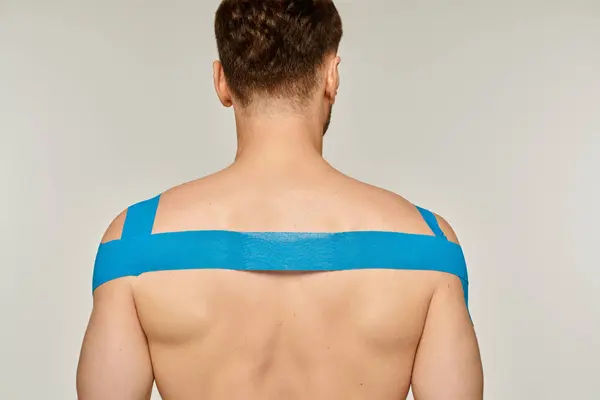 Vista posterior de modelo masculino atlético posando con cintas cinesiológicas en sus hombros y espalda - foto de stock