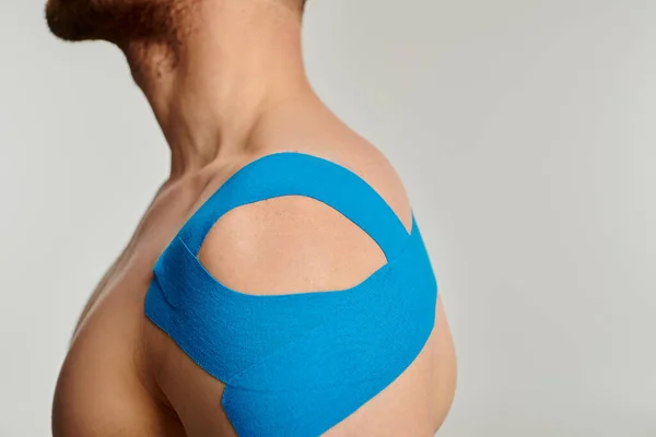 Cropped view of man with kinesiological tapes on his shoulder posing in profile on gray backdrop — Stock Photo