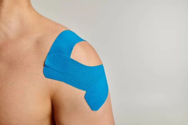 Cropped view of man with blue kinesiological tapes on his shoulder posing on gray background — Stock Photo