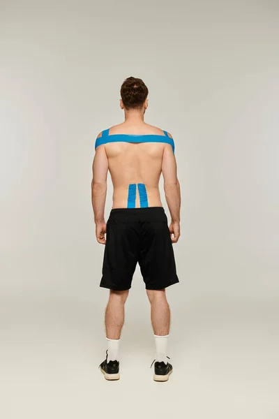 Back view of man in black sport pants with kinesiological tapes on his body on gray backdrop — Stock Photo