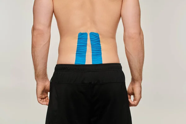 Cropped view of man in black sport pants with kinesiological tapes on his back on gray backdrop — Stock Photo