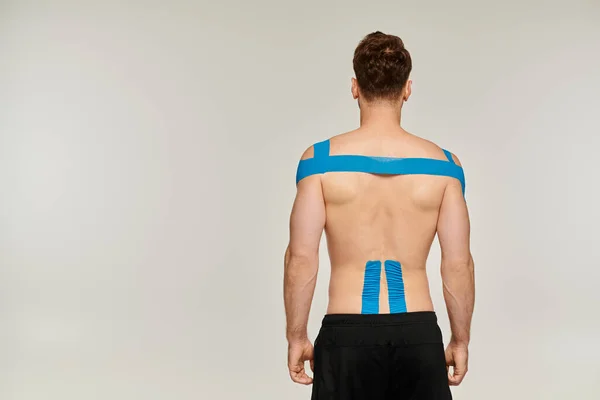 Back view of man in sport pants with kinesiological tapes on his back and shoulder on gray backdrop — Stock Photo
