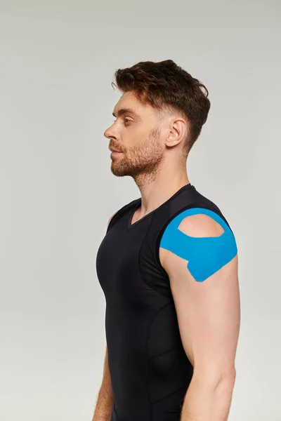 Good looking bearded man in sport wear with kinesiological tapes on his shoulder looking away — Stock Photo