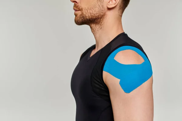 Cropped view of bearded man in black sport outfit with kinesiological tapes on his shoulder — Stock Photo