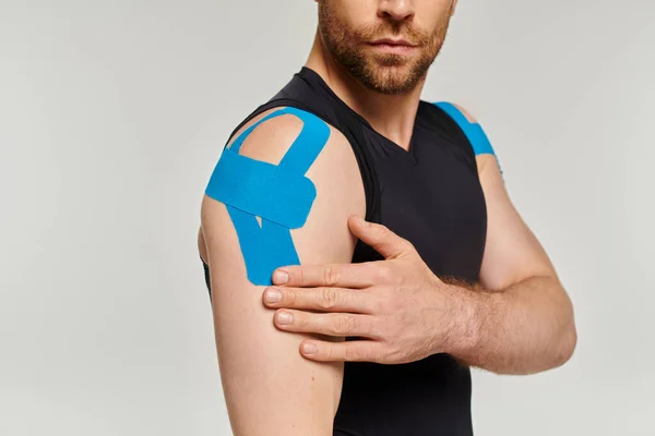 Visão cortada do homem barbudo em traje esporte preto tocando fita cinesiológica em seu ombro — Fotografia de Stock