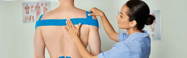 Cropped view of attractive doctor in medical costume putting kinesiological tapes on her patient — Stock Photo