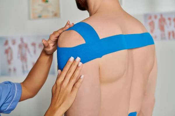 Cropped view of bearded patient on appointment while his doctor putting kinesiological tapes — Stock Photo