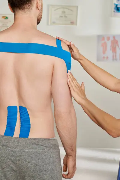 Cropped view of male patient during appointment while his doctor putting kinesio tapes on him — Stock Photo