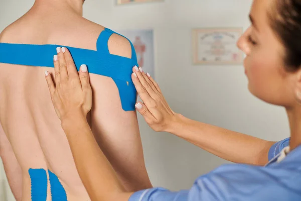 Visão cortada de jovem médico colocando fitas cinesiológicas azuis em seu paciente, cuidados de saúde — Fotografia de Stock