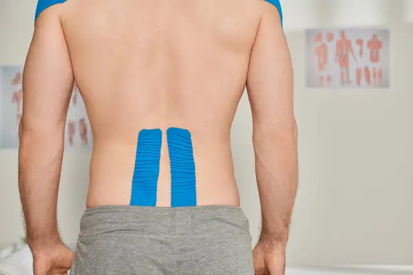 Cropped back view of man in gray sweatpants with kinesiological tapes on his back, healthcare — Stock Photo