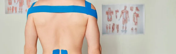 Vista recortada del paciente masculino en el consultorio médico con cintas de kinesio en la espalda y los hombros, pancarta - foto de stock
