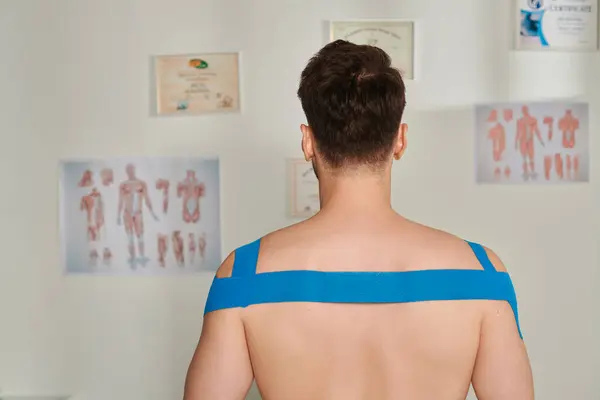 Задний вид человека с кинезиологическими лентами на плечах и спине во время приема, здравоохранение — стоковое фото