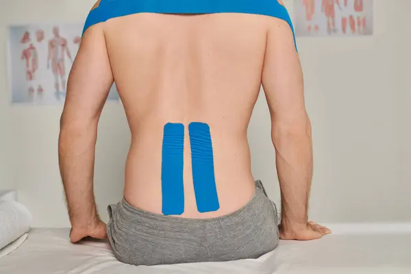 Vista recortada del hombre sentado durante la cita con cintas kinesiológicas en la espalda, atención médica - foto de stock