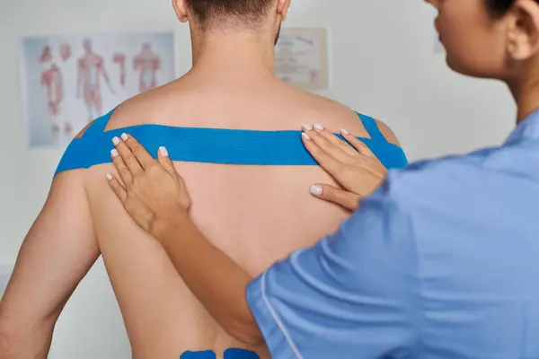 Visão cortada de jovem médica colocando fita cinesiológica nas costas de seu paciente, cuidados de saúde — Fotografia de Stock
