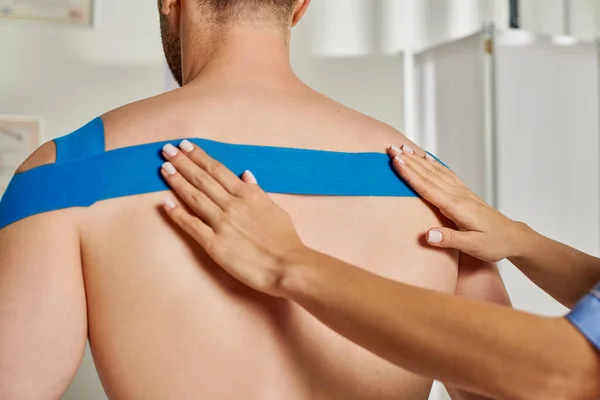 Visão recortada das mãos do jovem médico colocando fita cinesiológica nas costas de seu paciente masculino — Fotografia de Stock