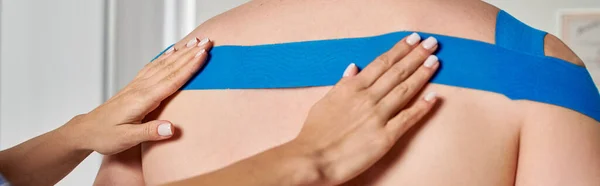 Cropped view of hands of female doctor putting kinesiological tape on back of her patient, banner — Stock Photo
