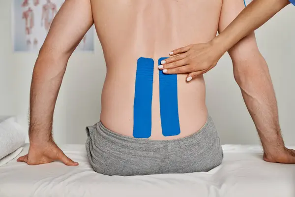 Cropped view of hand of young doctor on back of her patient with kinesiological tapes, healthcare — Stock Photo