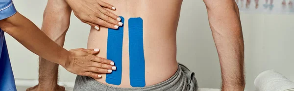 Cropped view of young female doctor putting kinesio tapes on back of her male patient, banner — Stock Photo