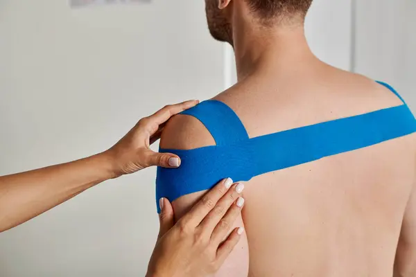Cropped view of young female doctor putting kinesiological tapes on her patient during appointment — Stock Photo