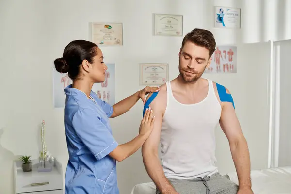 Handsome man in casual attire sitting while his young doctor putting kinesiological tapes on him — Stock Photo