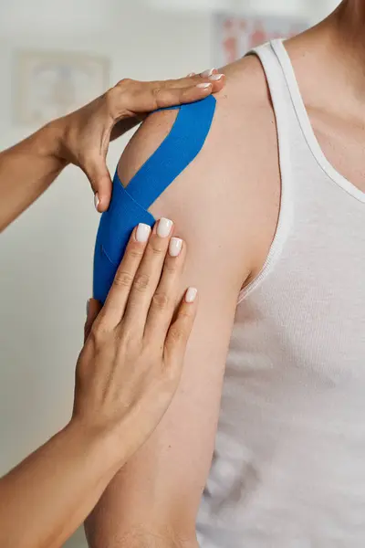 Cropped view of female young doctor putting kinesiological tape on shoulder of her male patient — Stock Photo
