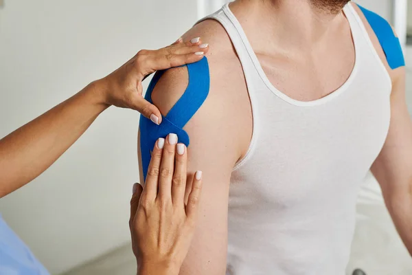 Cropped view of young doctor putting blue kinesiological tapes on her male patient, healthcare — Stock Photo