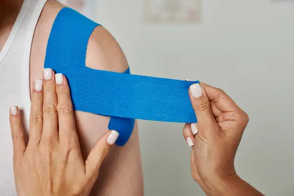 Vista recortada de la mano de la joven doctora poniendo cintas cinesiológicas en su paciente, cuidado de la salud - foto de stock