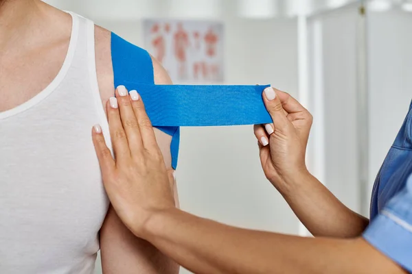 Cropped view of hand of young doctor putting blue kinesiological tapes on her patient, healthcare — Stock Photo