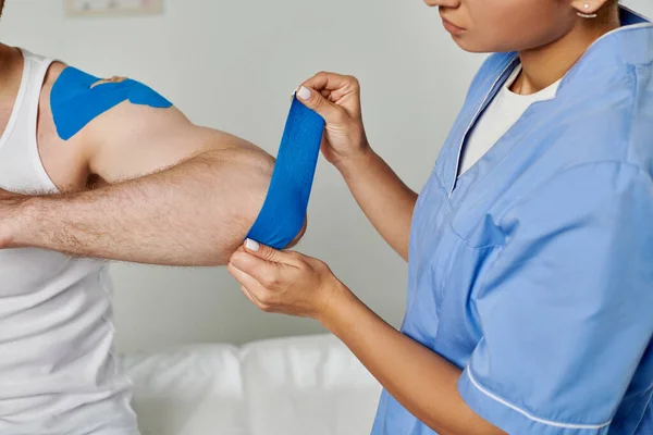 Vista cortada de médico fêmea em traje médico colocando fita cinesiológica no cotovelo de seu paciente — Fotografia de Stock