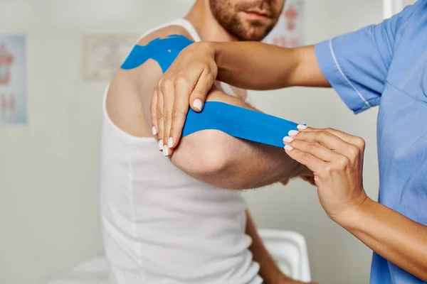 Cropped view of female doctor putting kinesio tape on elbow of her bearded patient, healthcare — Stock Photo