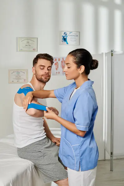Atractiva joven médico en traje médico poniendo cinta de kinesio en su paciente guapo, cuidado de la salud - foto de stock
