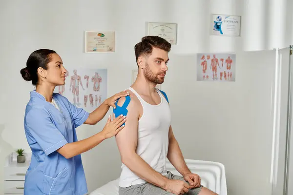 Handsome bearded man sitting during appointment while his doctor putting kinesio tapes on him — Stock Photo