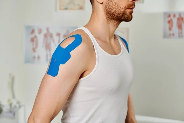 Обрезанный вид бородатого человека в повседневной одежде с кинезиологическими лентами на плече, здравоохранение — стоковое фото