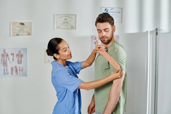 Atractivo joven médico consultando a su guapo paciente sobre cintas cinesiológicas, atención médica - foto de stock