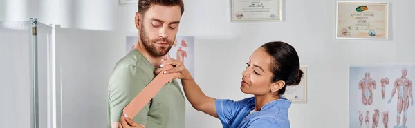 Красивий лікар консультує свого гарного пацієнта про кінезіологічні стрічки, охорону здоров'я, банер — стокове фото