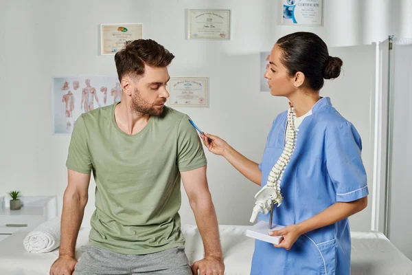 Atractivo médico sosteniendo modelo de columna vertebral y consultar a su paciente durante la cita, atención médica - foto de stock