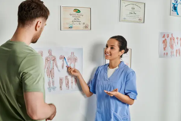 Cheerful female doctor showing anatomy schemes to her handsome bearded patient, healthcare — Stock Photo