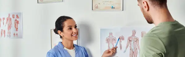 Freudige Ärztin in medizinischem Kostüm, die ihrem Patienten anatomische Schemata zeigt, Gesundheitswesen, Banner — Stockfoto