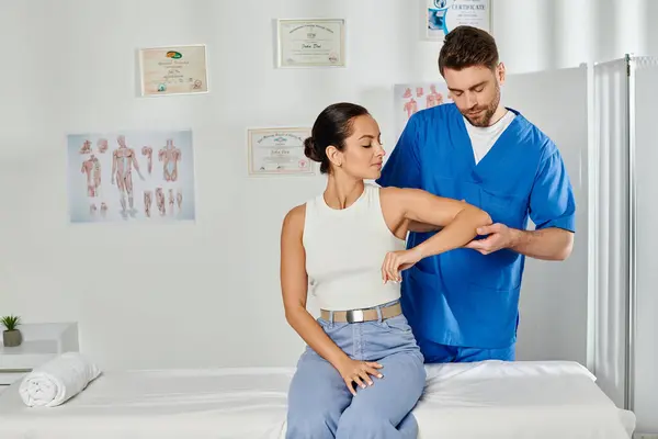 Médico bonito em traje médico olhando para o cotovelo de seu jovem paciente atraente, cuidados de saúde — Fotografia de Stock