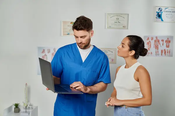 Attraente paziente femminile guardando il suo medico barbuto con il computer portatile in mano, assistenza sanitaria — Foto stock