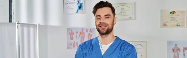 Cheerful good looking doctor with beard posing in his office and smiling at camera, banner — Stock Photo