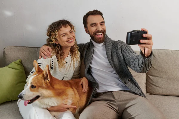 Couple smiling and taking photo on camera with corgi dog in modern apartment, happy moments — Stock Photo