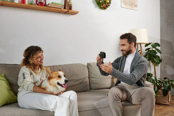 Man smiling and taking photo of wife with corgi dog on camera in modern apartment, happy moments — Stock Photo