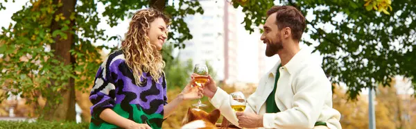 Happy couple clinking glasses of wine while sitting on grass and having picnic with corgi, banner — Stock Photo