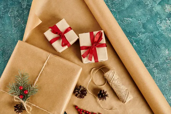 Прикрашені подарункові коробки поблизу соснових шишок і шпагат з ремісничим папером на синьому фоні, різдвяні ремесла — стокове фото