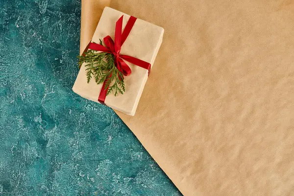 Gift box with red ribbon and green juniper branch on wrapping paper and blue textures backdrop — Stock Photo